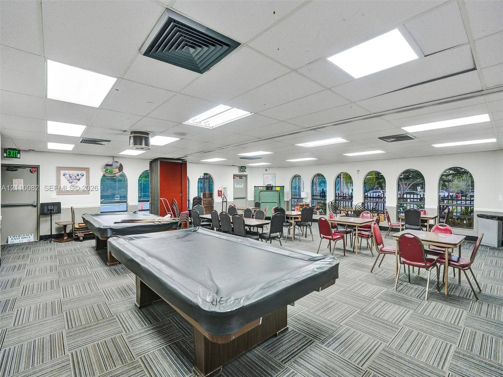 Large multipurpose room featuring a drop ceiling with integrated rectangular lighting, carpet tile flooring, and multiple arched windows