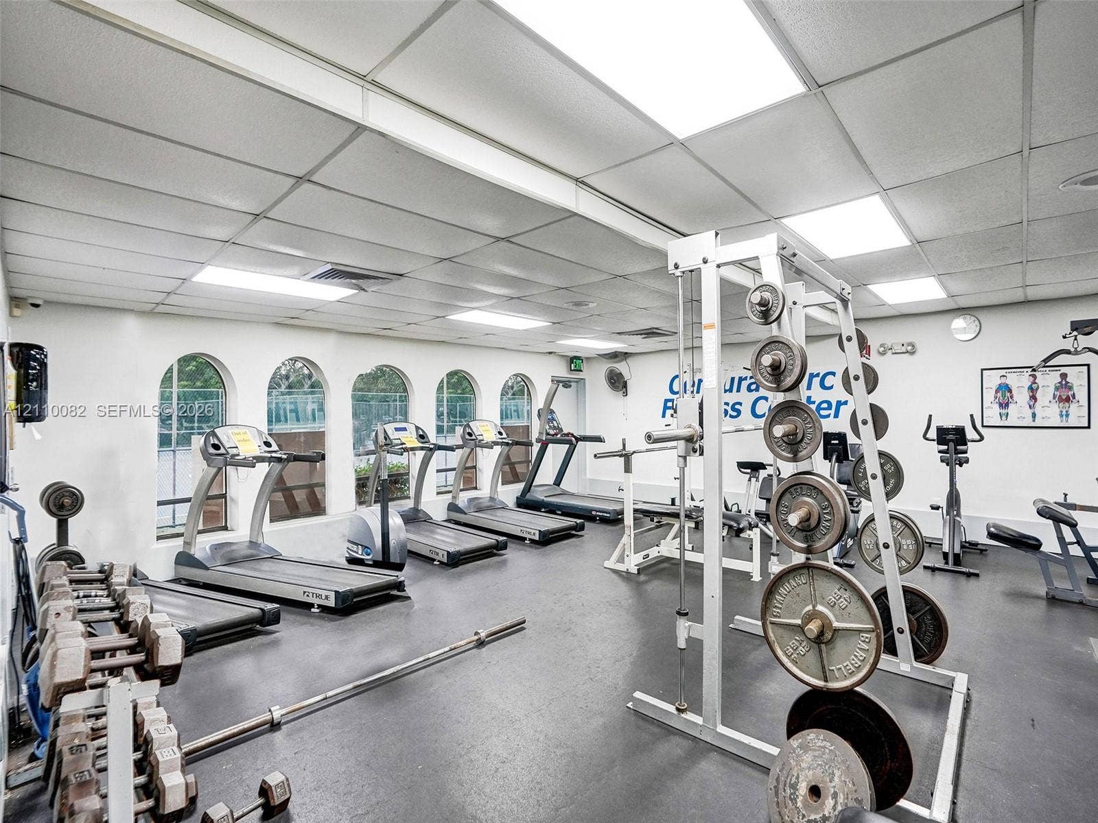 Fitness center featuring recessed lighting, a grid ceiling system, durable rubberized flooring, and multiple arched windows
