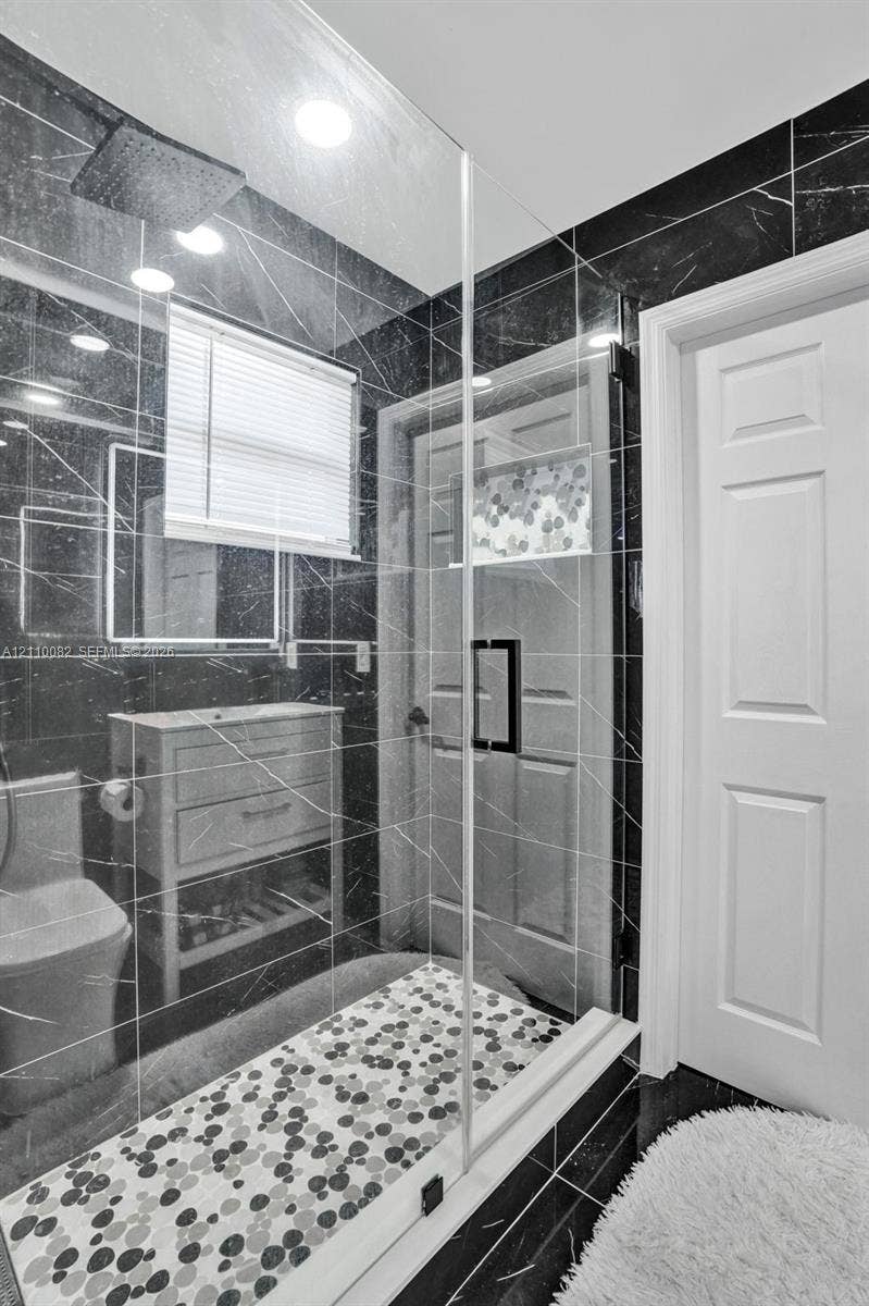 Walk-in shower enclosure featuring dark veined wall tile, a multi-textured stone-patterned floor, a built-in recessed wall niche, and a contemporary rain-style showerhead