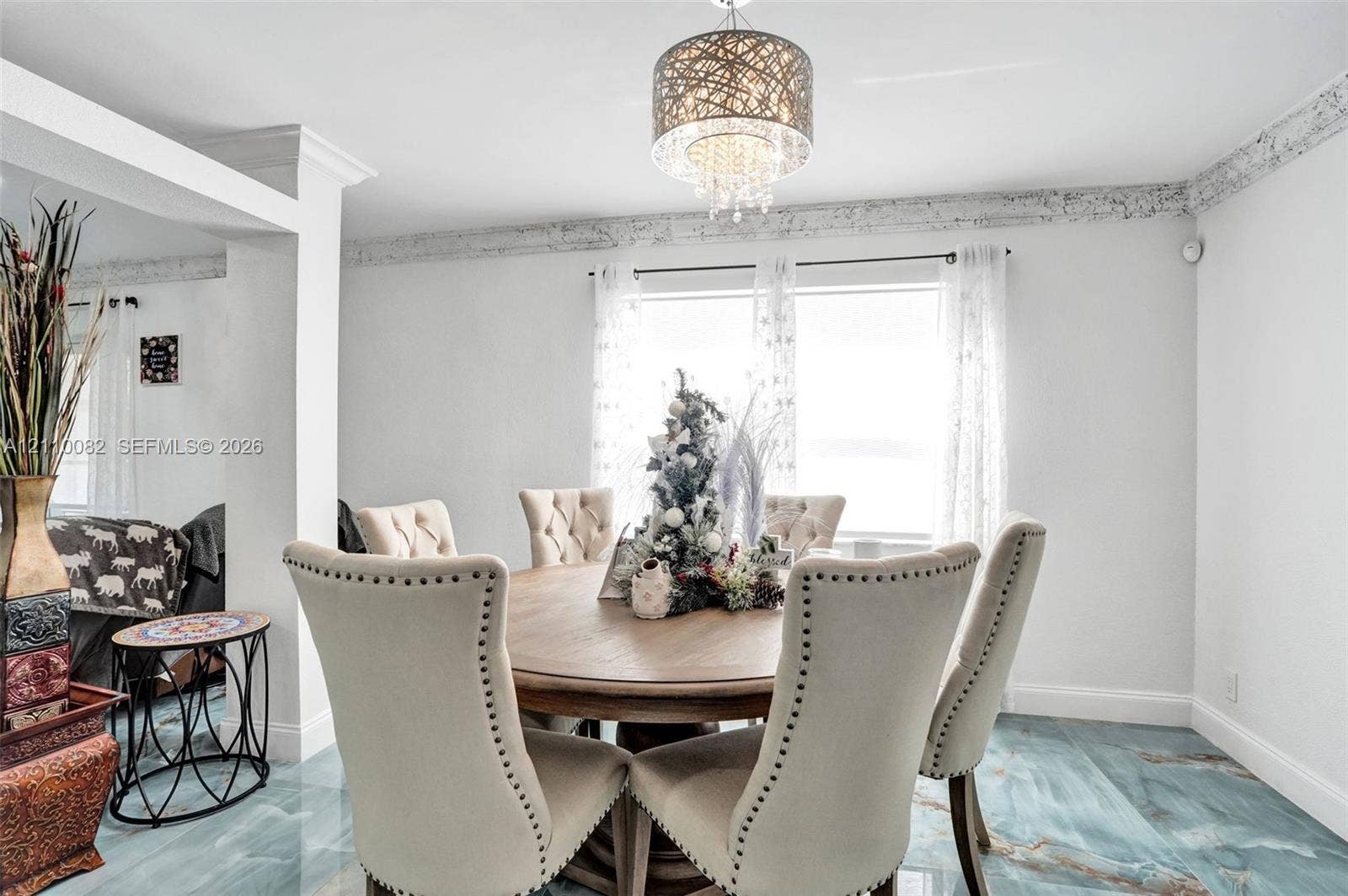 Dining area featuring large-format tile flooring, decorative crown molding, and a suspended multi-tiered crystal chandelier