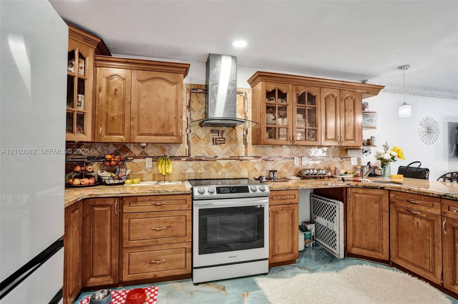 Kitchen featuring natural wood cabinetry with glass-panel upper doors, stone-surface countertops, decorative tile backsplash, stainless steel range, and a wall-mounted stainless steel chimney-style range hood
