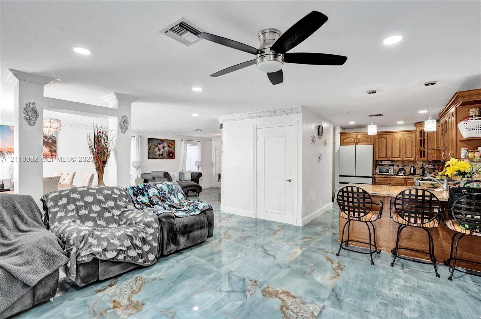 Open-concept interior featuring large-format polished stone flooring, custom wood cabinetry, recessed lighting, and a multi-blade ceiling fan
