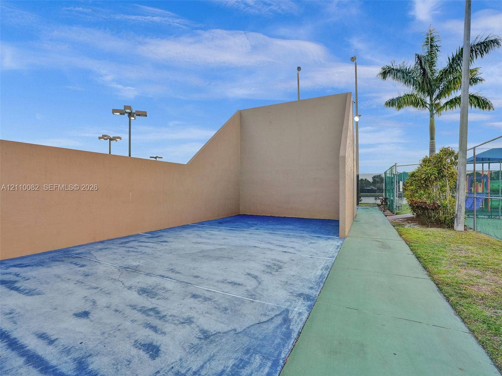 Recreational handball court featuring a solid wall surface, blue-toned court flooring, integrated lighting fixtures, and perimeter fencing