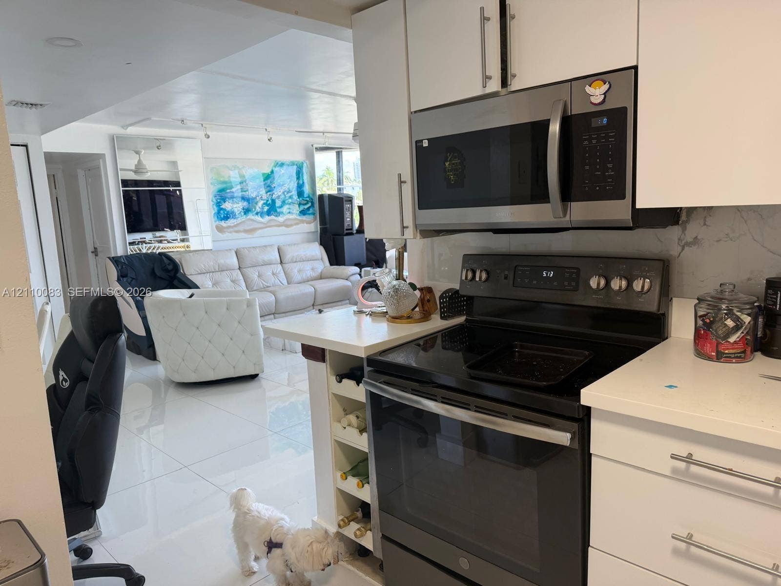 Kitchen featuring white cabinetry, light-toned stone-finish countertops, stainless steel microwave, black electric range, and integrated wine storage shelving