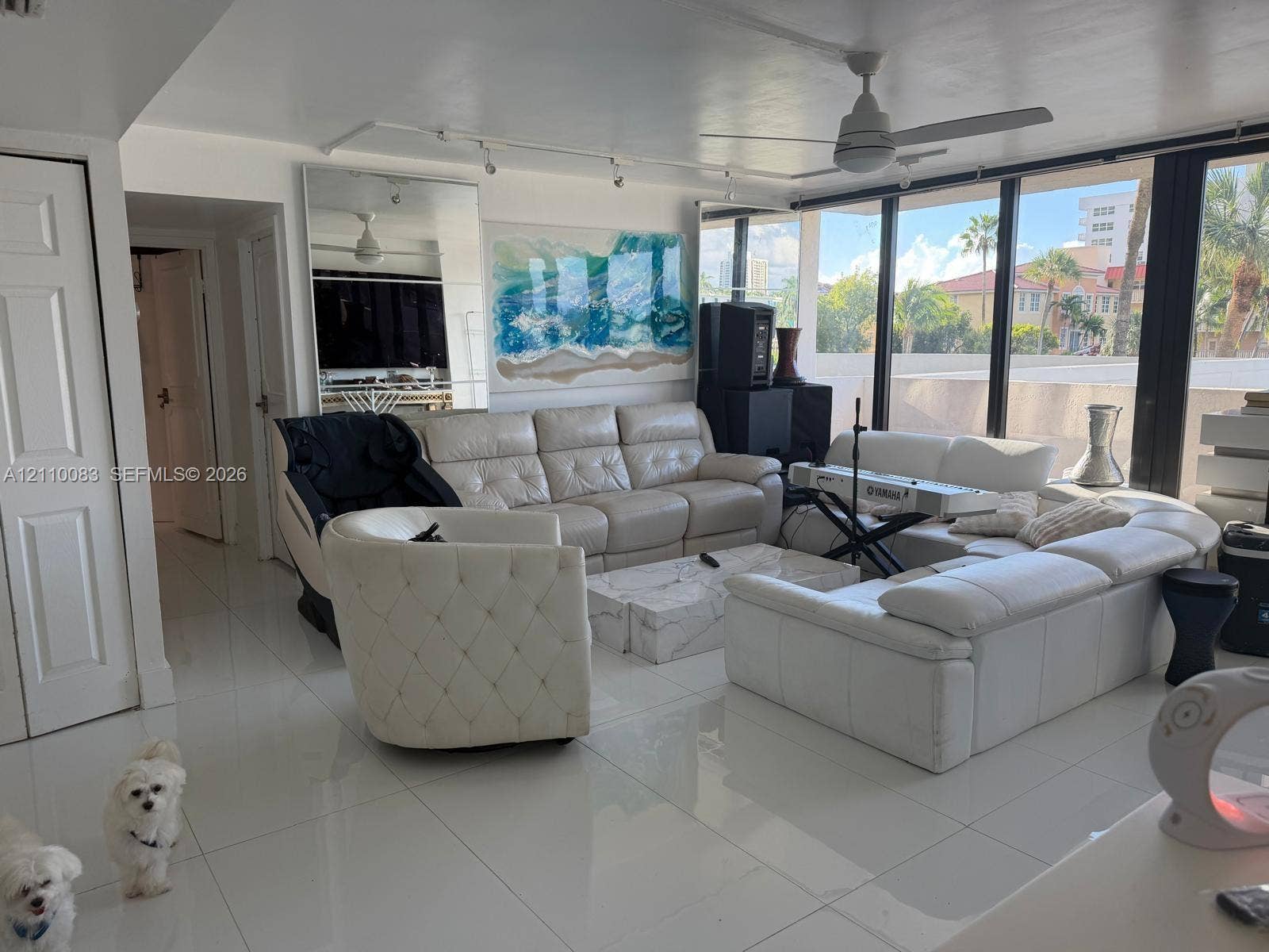 Living area featuring large-format tile flooring, floor-to-ceiling windows, full-length wall mirror, ceiling fan, and adjustable track lighting