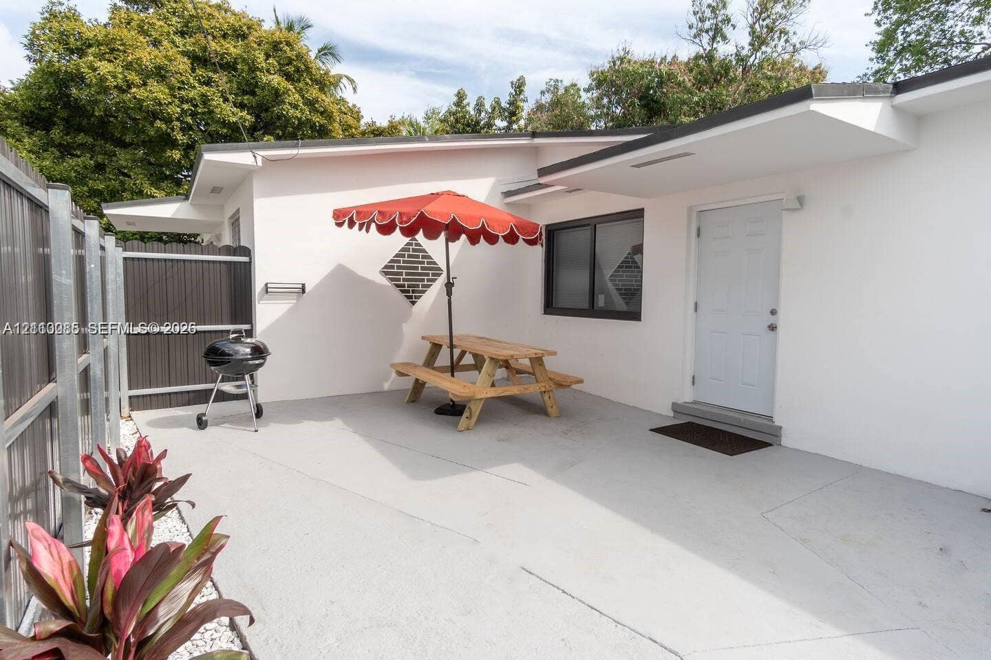 7815 NW 5th Court, #1, Miami, Miami, FL 33150 Concrete patio featuring a vertical wood-slat privacy fence, exterior white stucco siding, and dark-trimmed window frames