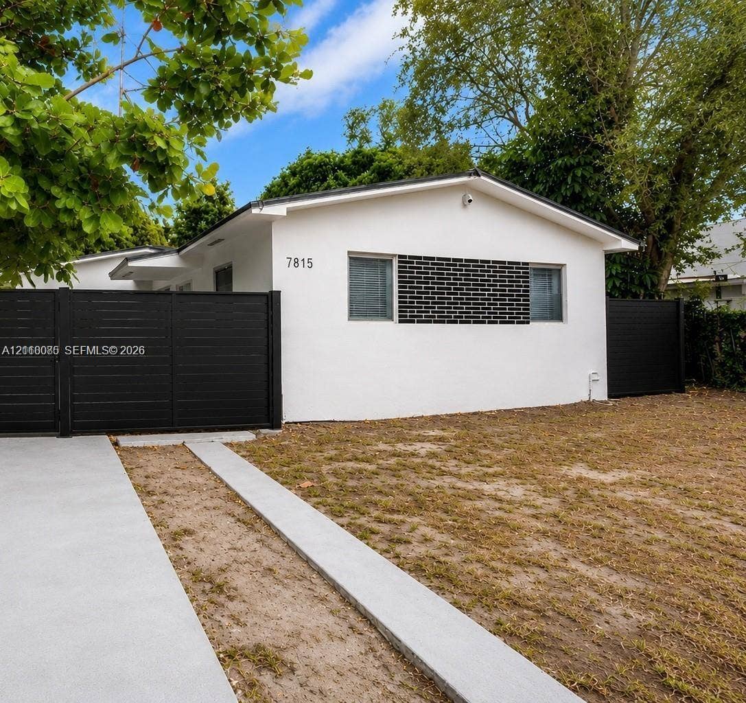7815 NW 5th Court, #1, Miami, Miami, FL 33150 Exterior featuring white stucco siding, contrasting black brick masonry accents, dark horizontal privacy fencing, and a concrete driveway