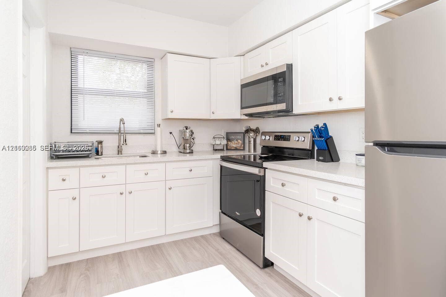 7815 NW 5th Court, #1, Miami, Miami, FL 33150 Kitchen featuring white Shaker-style cabinetry, solid-surface countertops, wood-finish flooring, and stainless steel appliances including a built-in microwave and range