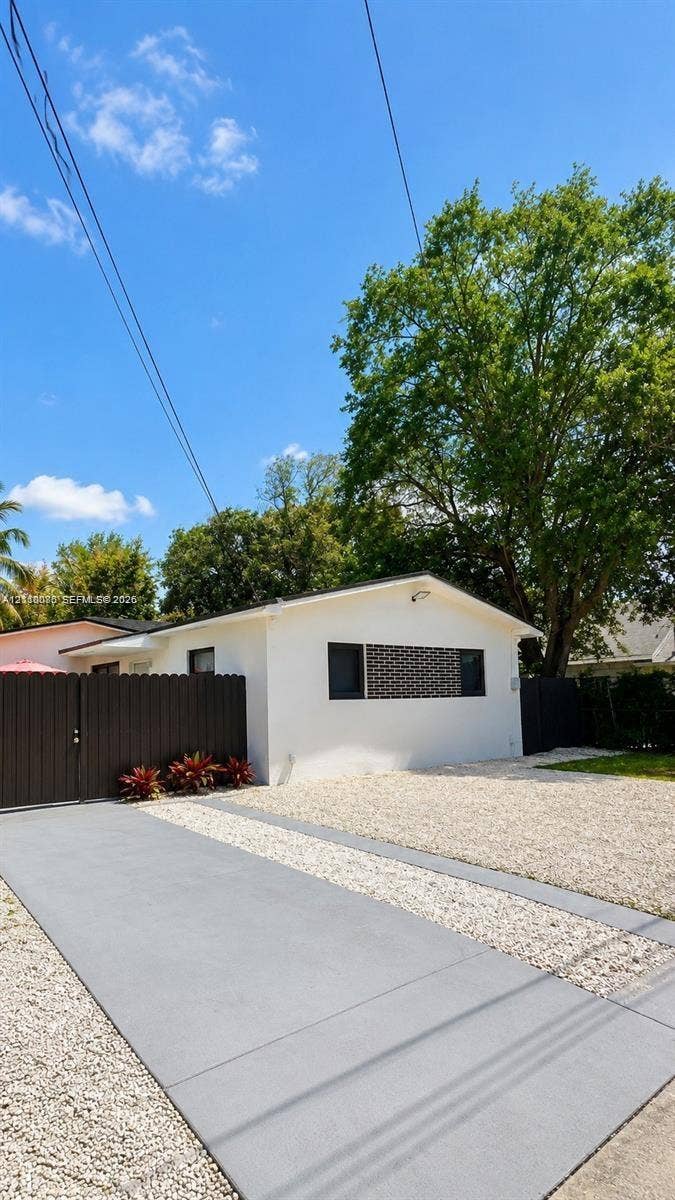 7815 NW 5th Court, #1, Miami, Miami, FL 33150 Exterior featuring white stucco siding, a concrete ribbon driveway, decorative privacy fencing, and a gravel front courtyard