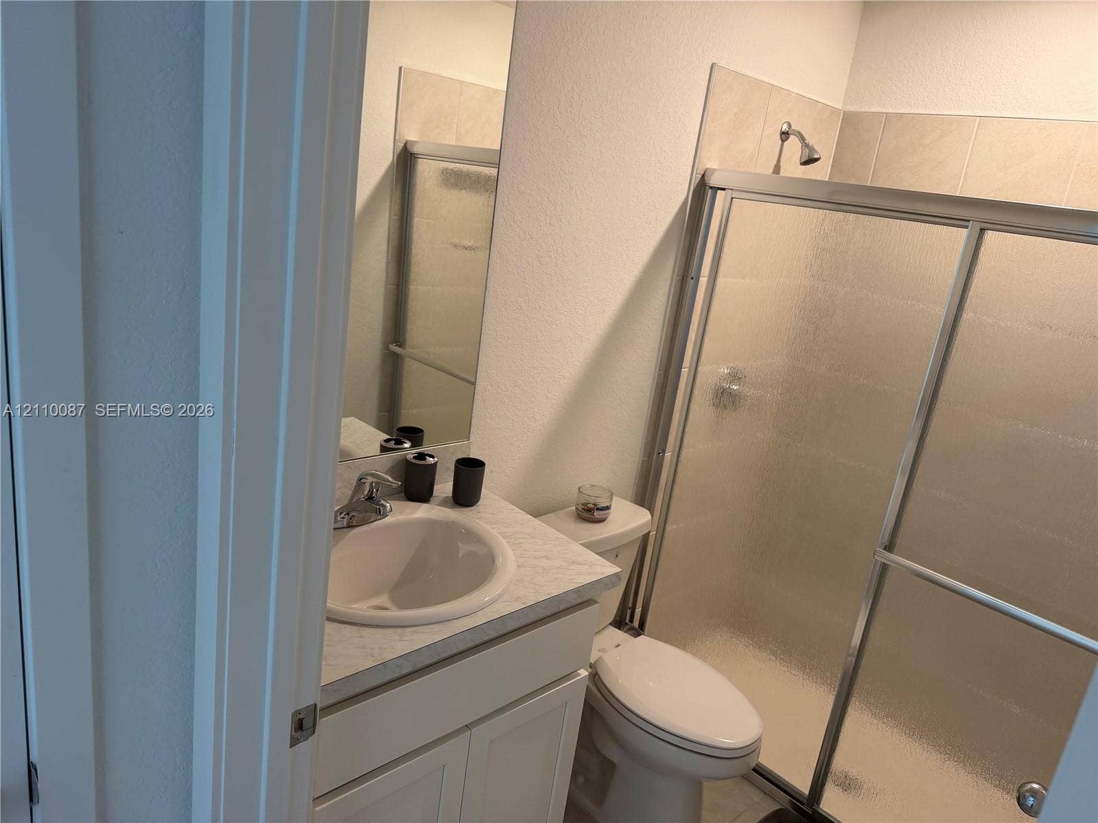 1358 NE 3rd Avenue, #1, Florida City, Florida City, FL 33034 Bathroom featuring a single-sink vanity with a stone-composite countertop, chrome faucet hardware, and a shower enclosure with sliding textured glass doors and tile surround