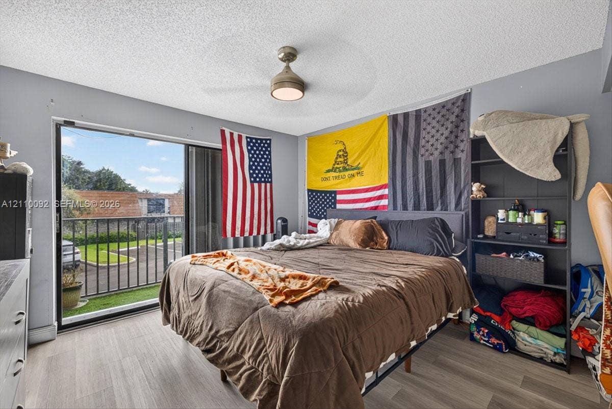 1403 SW 110th Way, Davie, FL 33324 Sliding glass door leading to a private balcony with metal railing, wood-finish flooring, and a ceiling-mounted light fixture with integrated fan