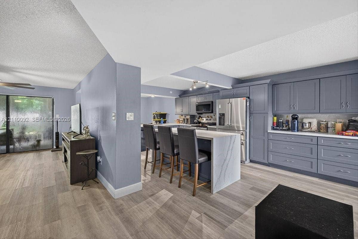 1403 SW 110th Way, Davie, FL 33324 Kitchen featuring gray shaker-style cabinetry, white waterfall-edge stone island, stainless steel appliances, and wood-finish flooring