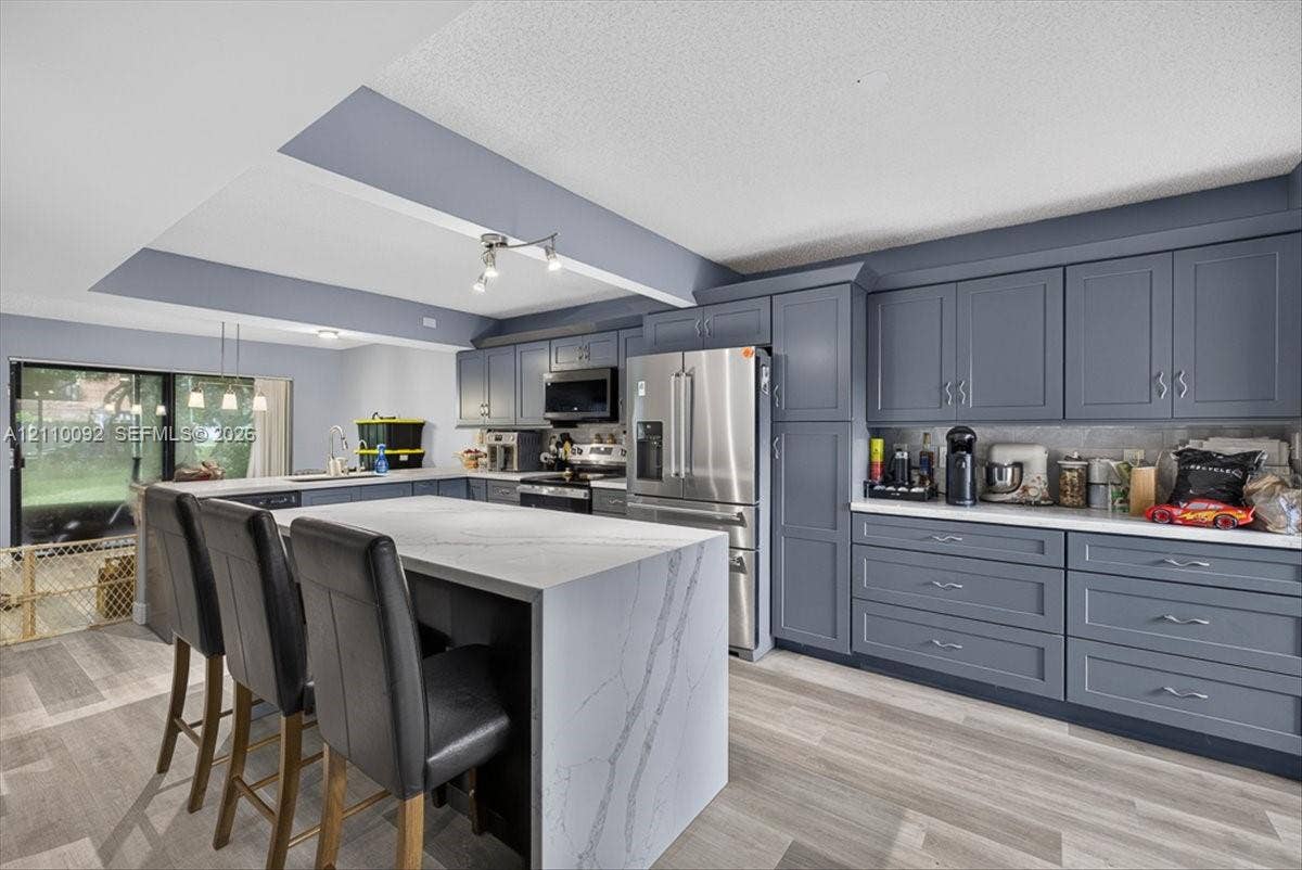 1403 SW 110th Way, Davie, FL 33324 Kitchen featuring shaker-style cabinetry, a waterfall-edge center island with quartz countertops, stainless steel appliances, and wood-finish flooring