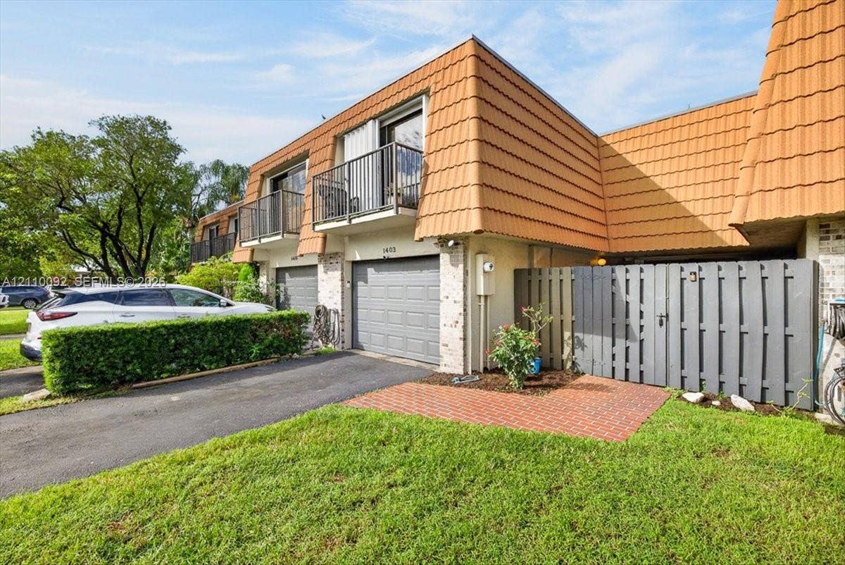 1403 SW 110th Way, Davie, FL 33324 Exterior facade featuring a mansard roof with ceramic tiles, integrated private balconies with metal railings, a brick-paved patio, and a privacy fence