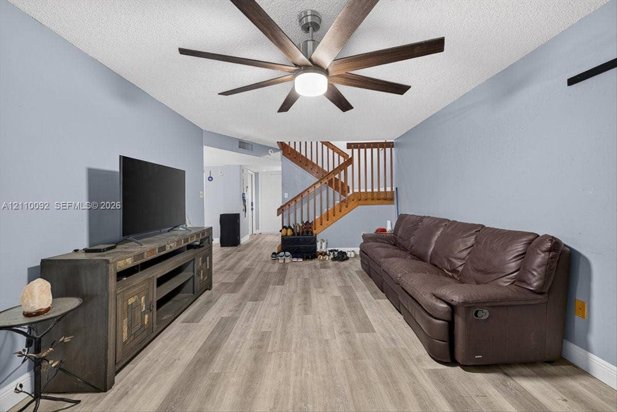 1403 SW 110th Way, Davie, FL 33324 Wood-finish flooring, multi-blade ceiling fan with integrated lighting, and wooden staircase featuring a slatted banister