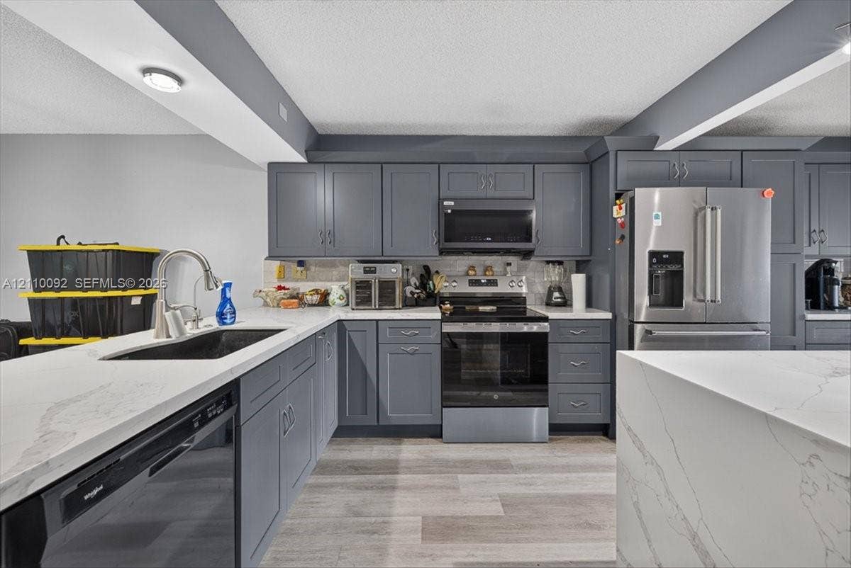 1403 SW 110th Way, Davie, FL 33324 Kitchen featuring charcoal-toned shaker cabinetry, quartz countertops with veining, stainless steel appliances, and wood-finish flooring