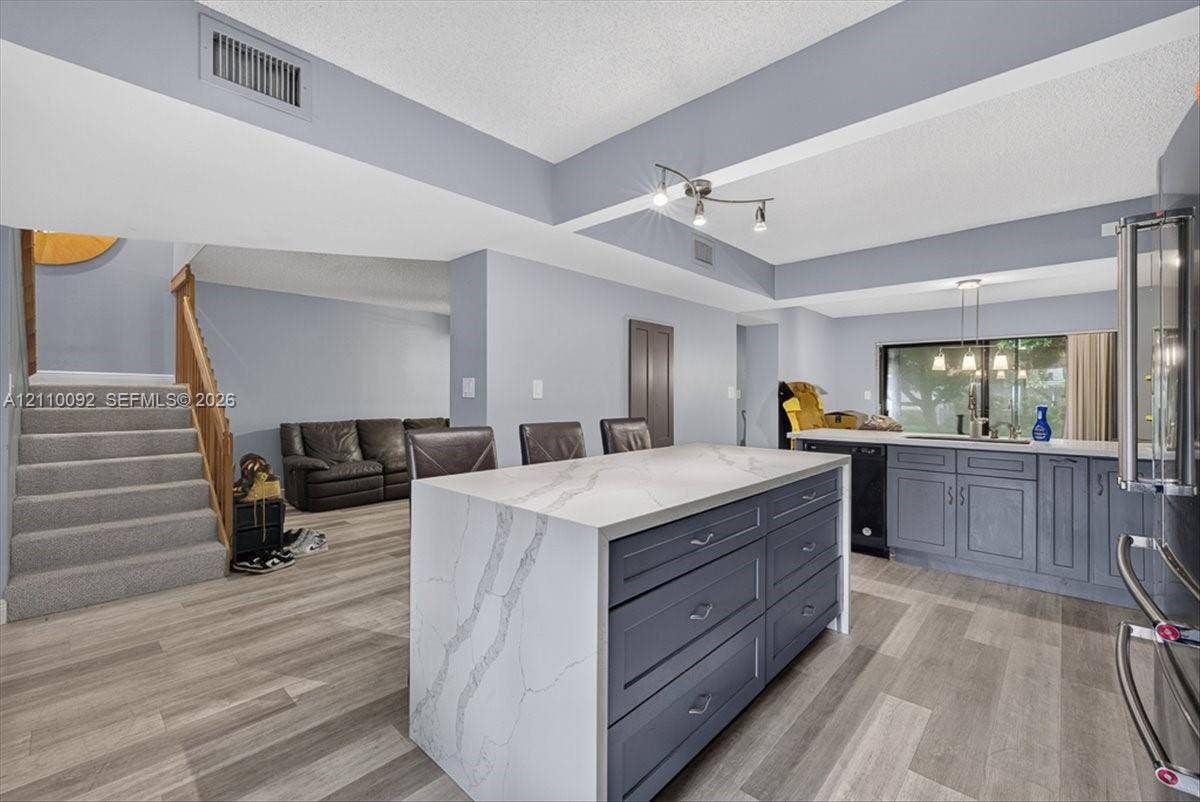 1403 SW 110th Way, Davie, FL 33324 Kitchen featuring an oversized island with a stone-finish waterfall countertop, dark cabinetry, wood-finish flooring, and multi-bulb pendant lighting