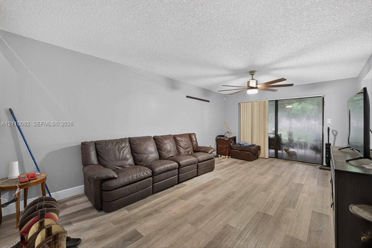 1403 SW 110th Way, Davie, FL 33324 Living space featuring wood-finish flooring, a multi-blade ceiling fan with integrated lighting, and a sliding glass door providing external access