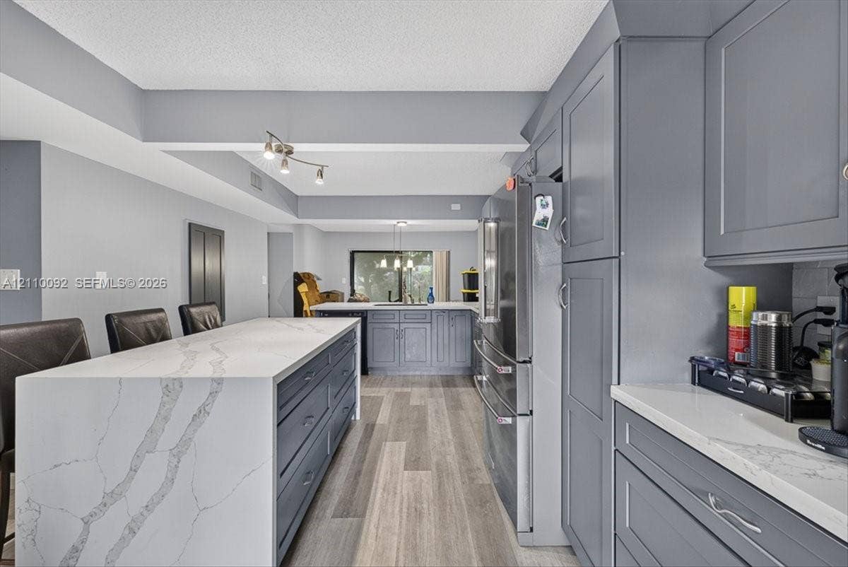 1403 SW 110th Way, Davie, FL 33324 Kitchen featuring gray cabinetry, waterfall-edge quartz countertops, stainless steel appliances, and wood-finish flooring