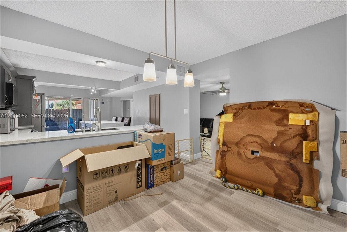 1403 SW 110th Way, Davie, FL 33324 Kitchen featuring a pass-through counter, stone-finish countertops, stainless steel undermount sink, three-light linear pendant fixture, and wood-finish flooring