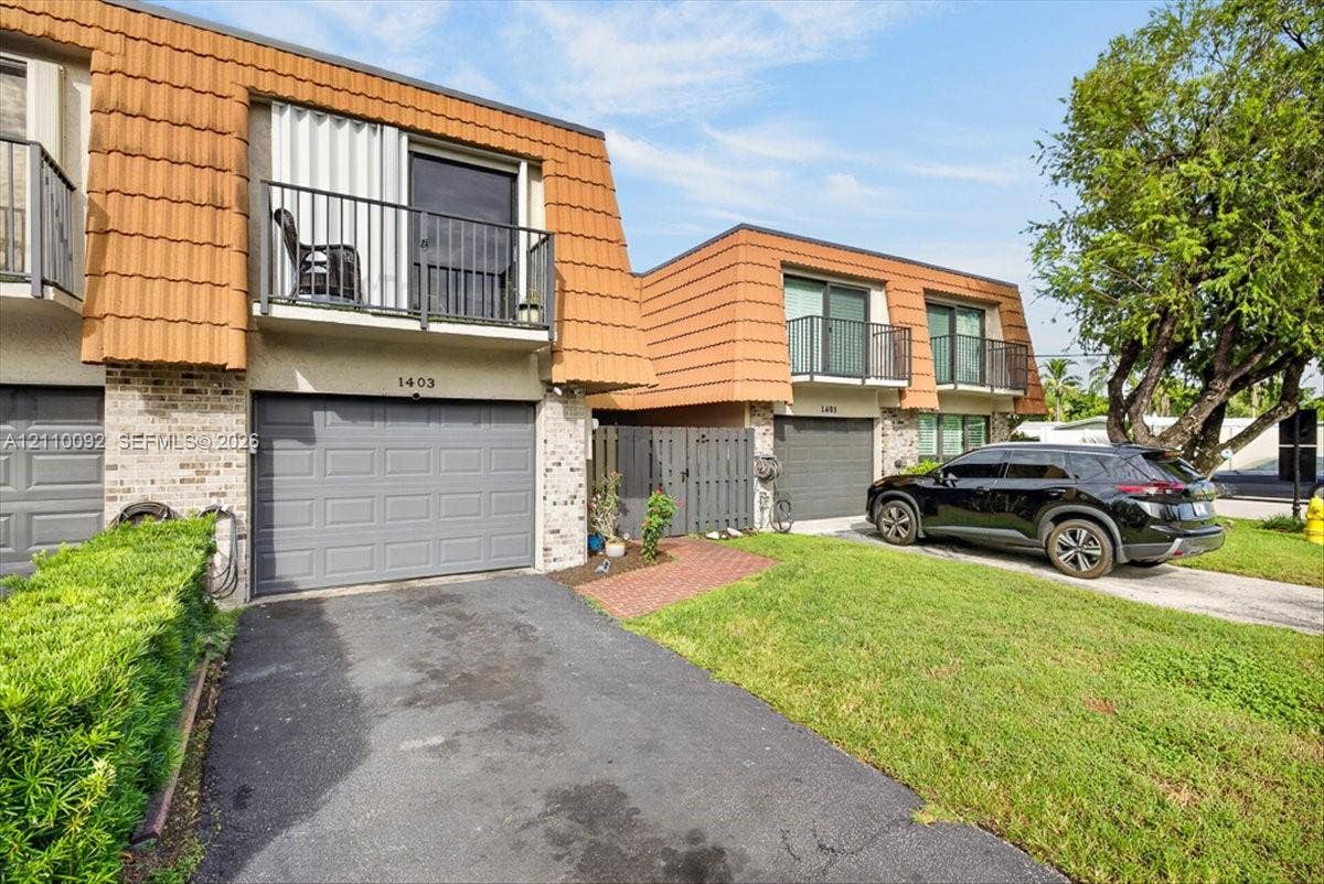 1403 SW 110th Way, Davie, FL 33324 Multi-level exterior featuring terra cotta tile mansard roofing, brick veneer siding, private upper-level balconies with metal railings, and attached single-car garages