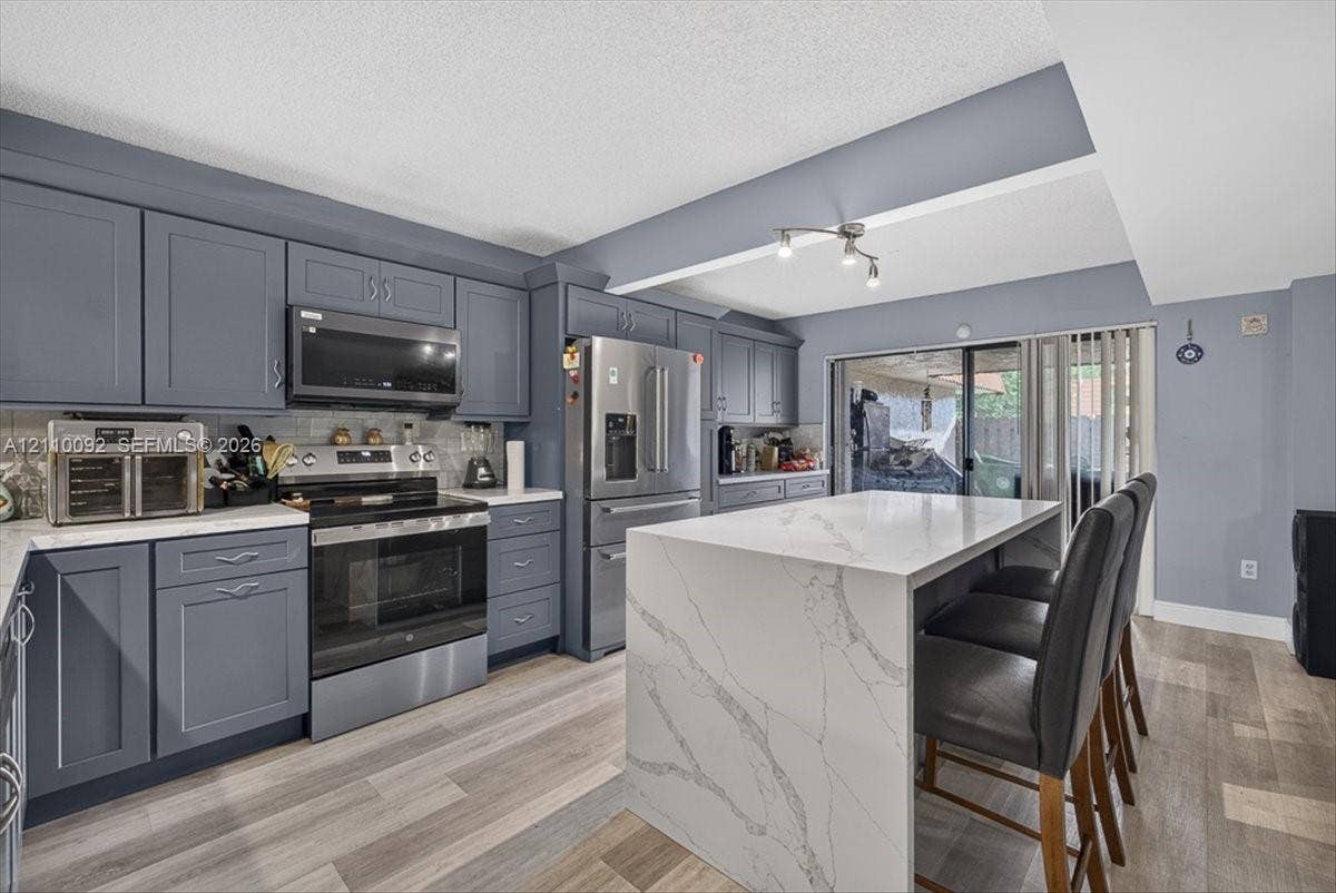 1403 SW 110th Way, Davie, FL 33324 Kitchen featuring shaker-style cabinetry, a waterfall-edge stone island, stainless steel appliances, and wood-finish flooring