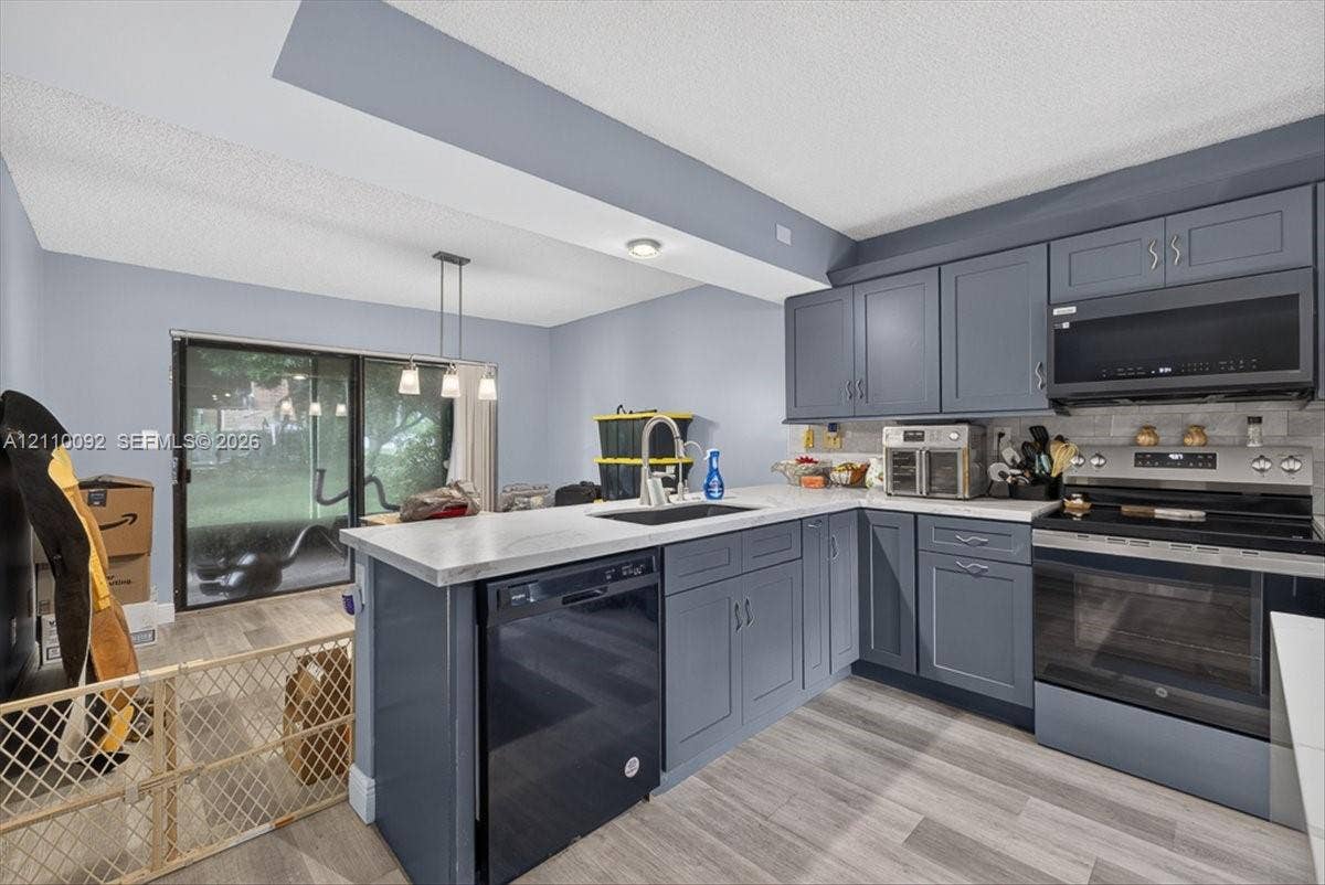 1403 SW 110th Way, Davie, FL 33324 Kitchen featuring charcoal-toned cabinetry, light-toned countertop, undermount sink, stainless steel appliance suite, and wood-finish flooring