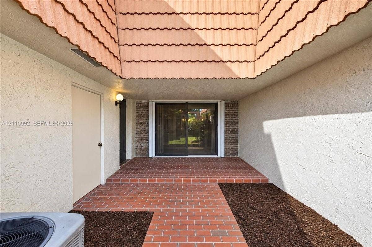 1403 SW 110th Way, Davie, FL 33324 Covered entrance featuring a brick-paved walkway, stucco exterior walls, a recessed brick-accented doorway with sliding glass panels, and a decorative tile-shingle roof overhang