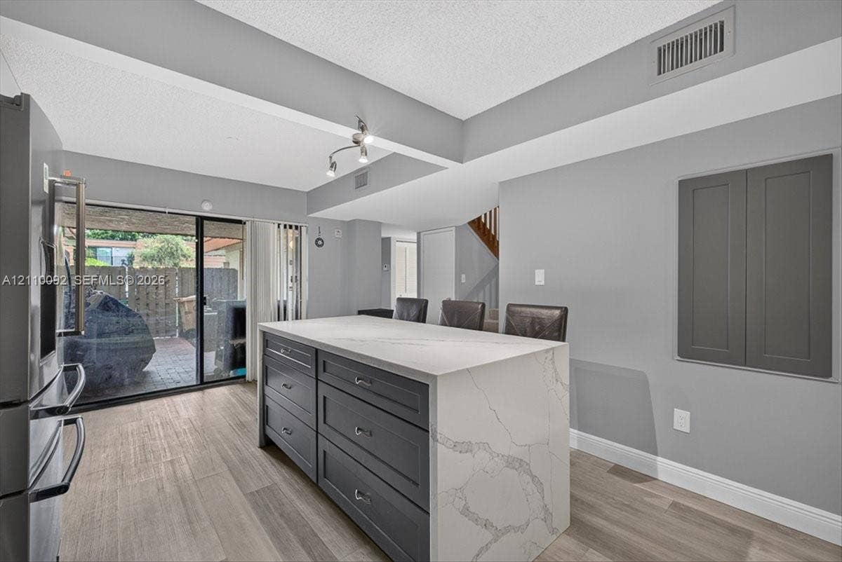 1403 SW 110th Way, Davie, FL 33324 Kitchen island featuring dark cabinetry, a waterfall-edge countertop with integrated drawers, wood-finish flooring, and sliding glass doors
