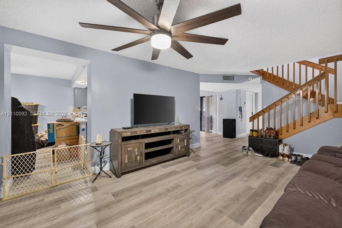 1403 SW 110th Way, Davie, FL 33324 Living area featuring wood-finish flooring, a multi-blade ceiling fan with integrated lighting, and a wooden staircase with balustrades