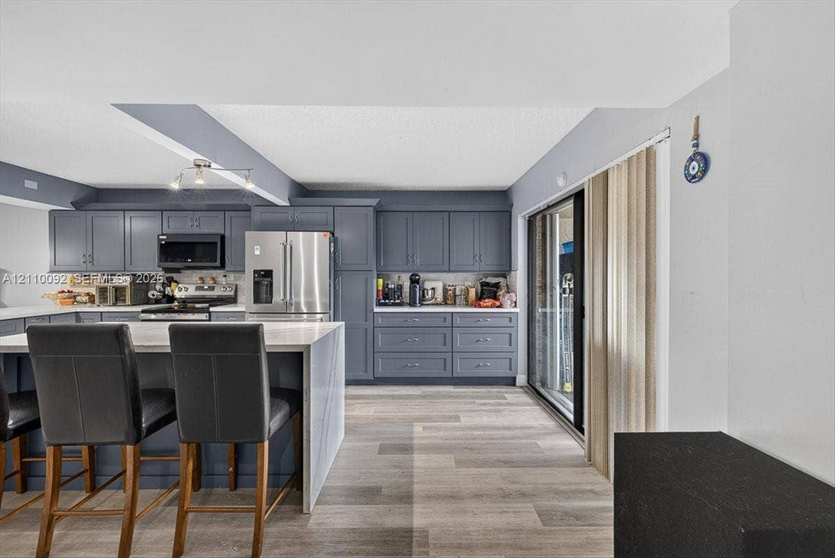 1403 SW 110th Way, Davie, FL 33324 Kitchen featuring slate-grey shaker cabinetry, quartz countertops, a central island with bar seating, stainless steel appliances, and wood-finish flooring