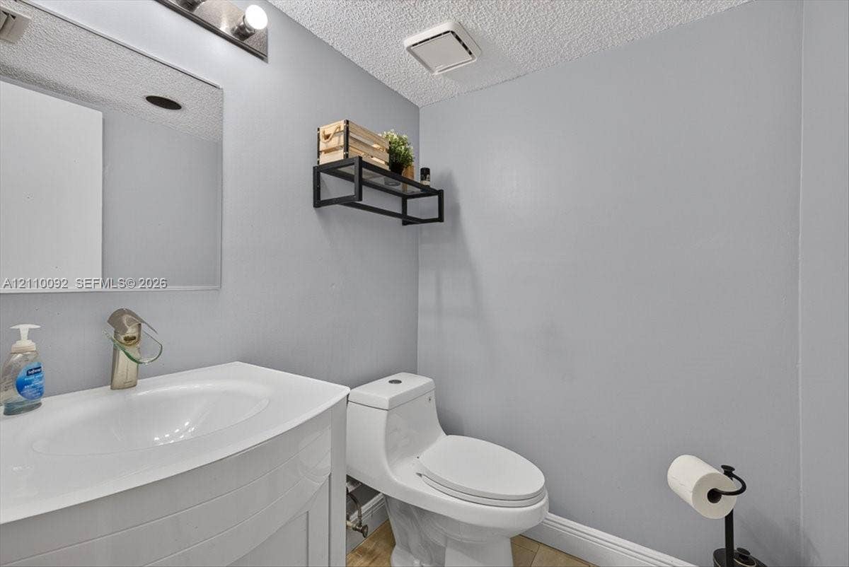 1403 SW 110th Way, Davie, FL 33324 Wall-mounted rectangular vanity with a white integrated basin, single-handle brushed nickel faucet, large frameless mirror, and dual-flush toilet