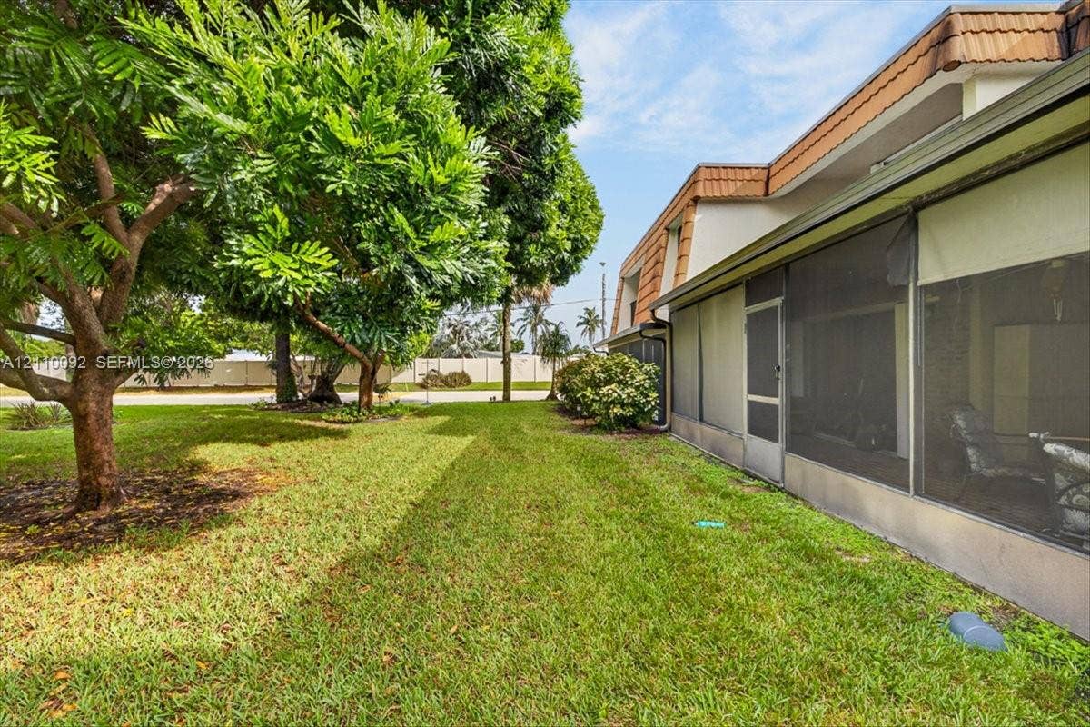 1403 SW 110th Way, Davie, FL 33324 Exterior side yard featuring a manicured lawn, mature trees, and a screened-in enclosure with metal framing
