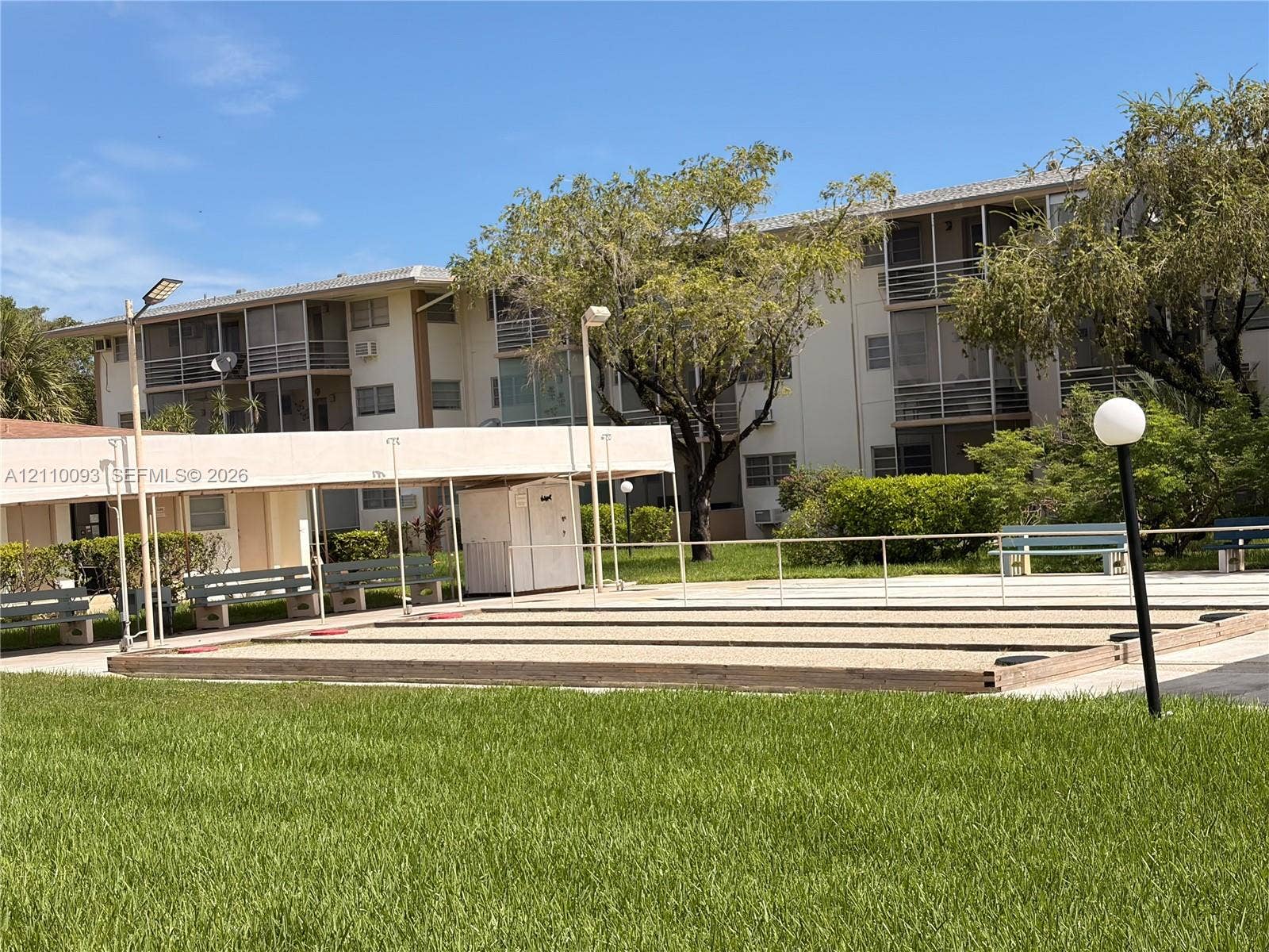 1395 NE 167th Street, #205, Miami, FL 33162 Outdoor shuffleboard court featuring a raked surface, covered seating area, perimeter lighting, and manicured lawn
