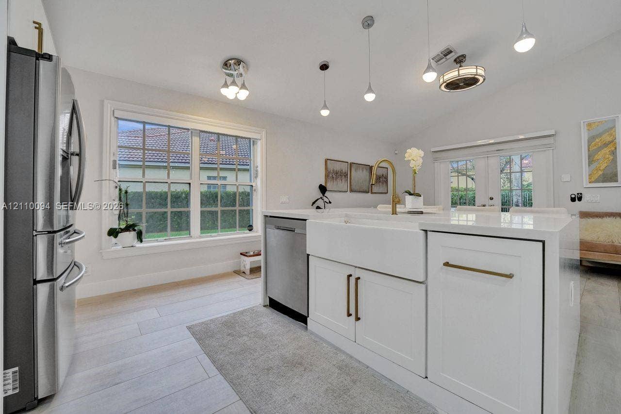 2064 Island Circle, Weston, FL 33326 Kitchen featuring an island with a white farmhouse sink, brass-tone hardware, stainless steel appliances, pendant lighting, and wood-finish flooring