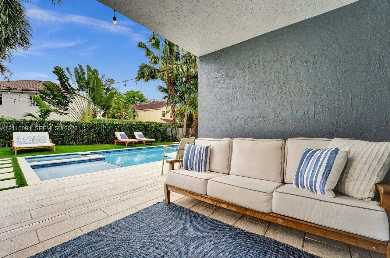 2064 Island Circle, Weston, FL 33326 Covered patio featuring a textured grey accent wall, stone-style pavers, and a built-in string lighting system overlooking a rectangular swimming pool with an integrated spa