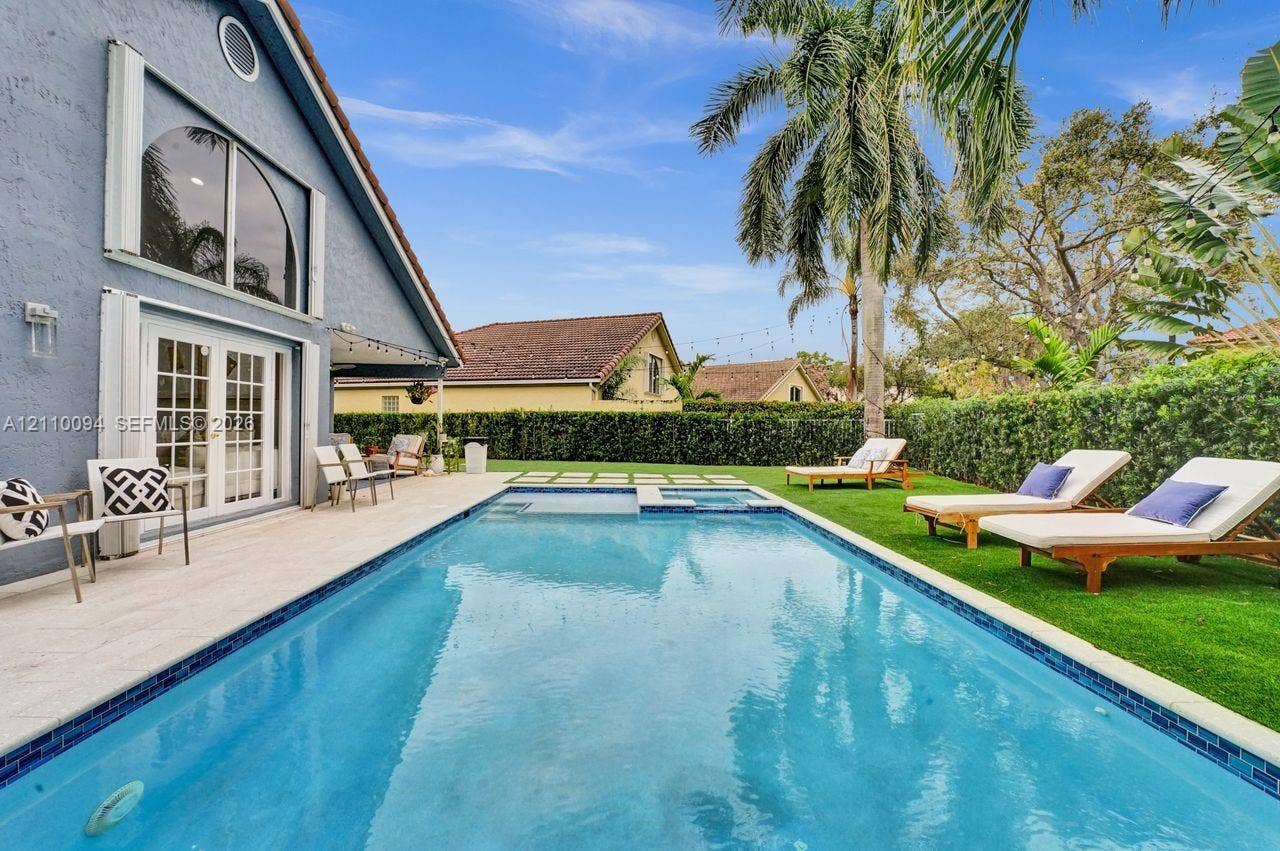 2064 Island Circle, Weston, FL 33326 Backyard featuring a rectangular swimming pool with a tiled waterline, integrated spa, stone-finish deck, manicured lawn, and mature palm tree
