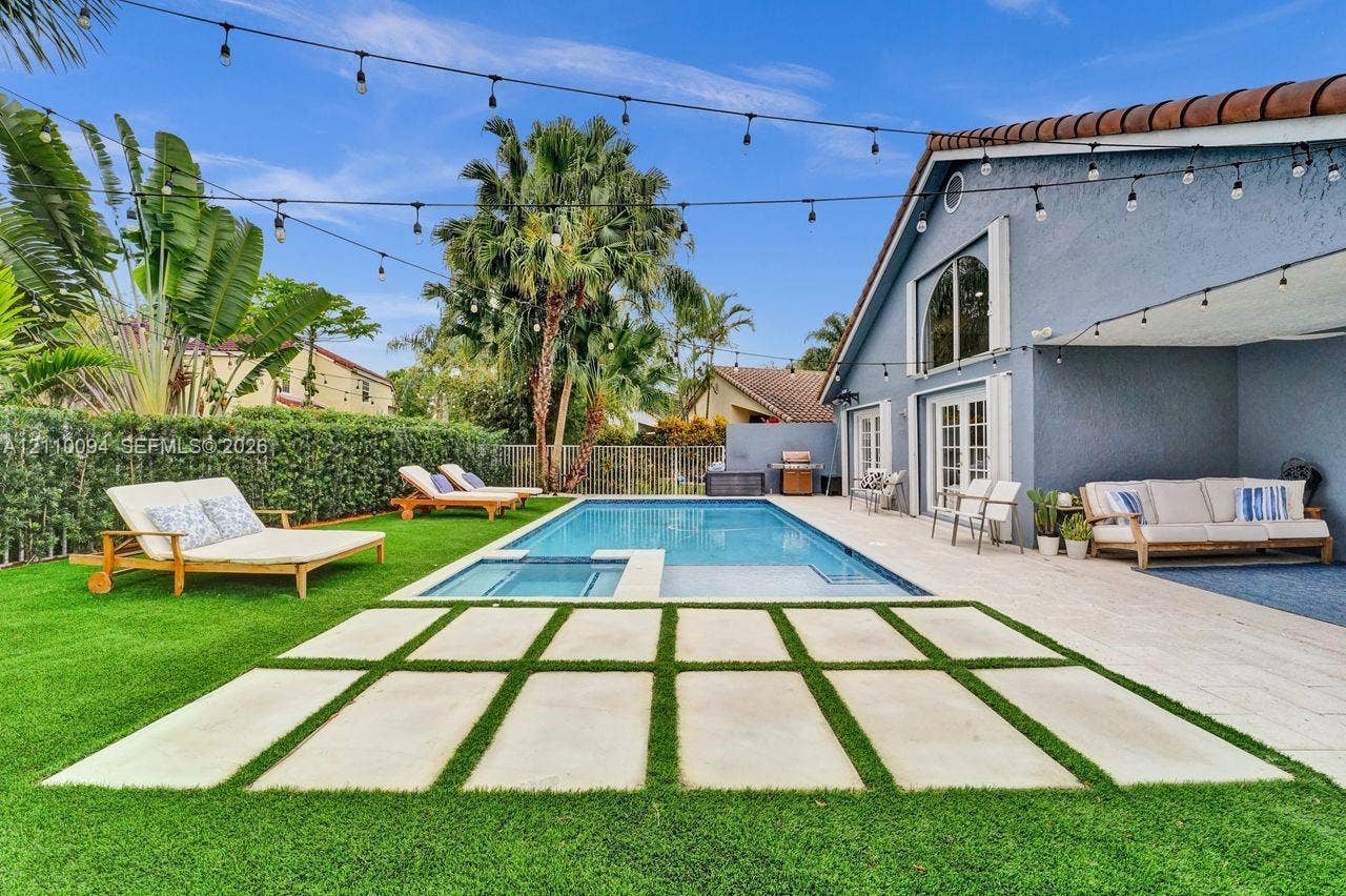 2064 Island Circle, Weston, FL 33326 Private backyard featuring an in-ground pool with a built-in spa, paved stone patio with grid inlay, synthetic lawn, and overhead string lighting