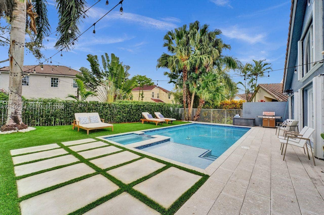 2064 Island Circle, Weston, FL 33326 Backyard featuring an in-ground swimming pool with an integrated spa, large-format paver patio, square concrete pavers set in turf, and mature palm trees