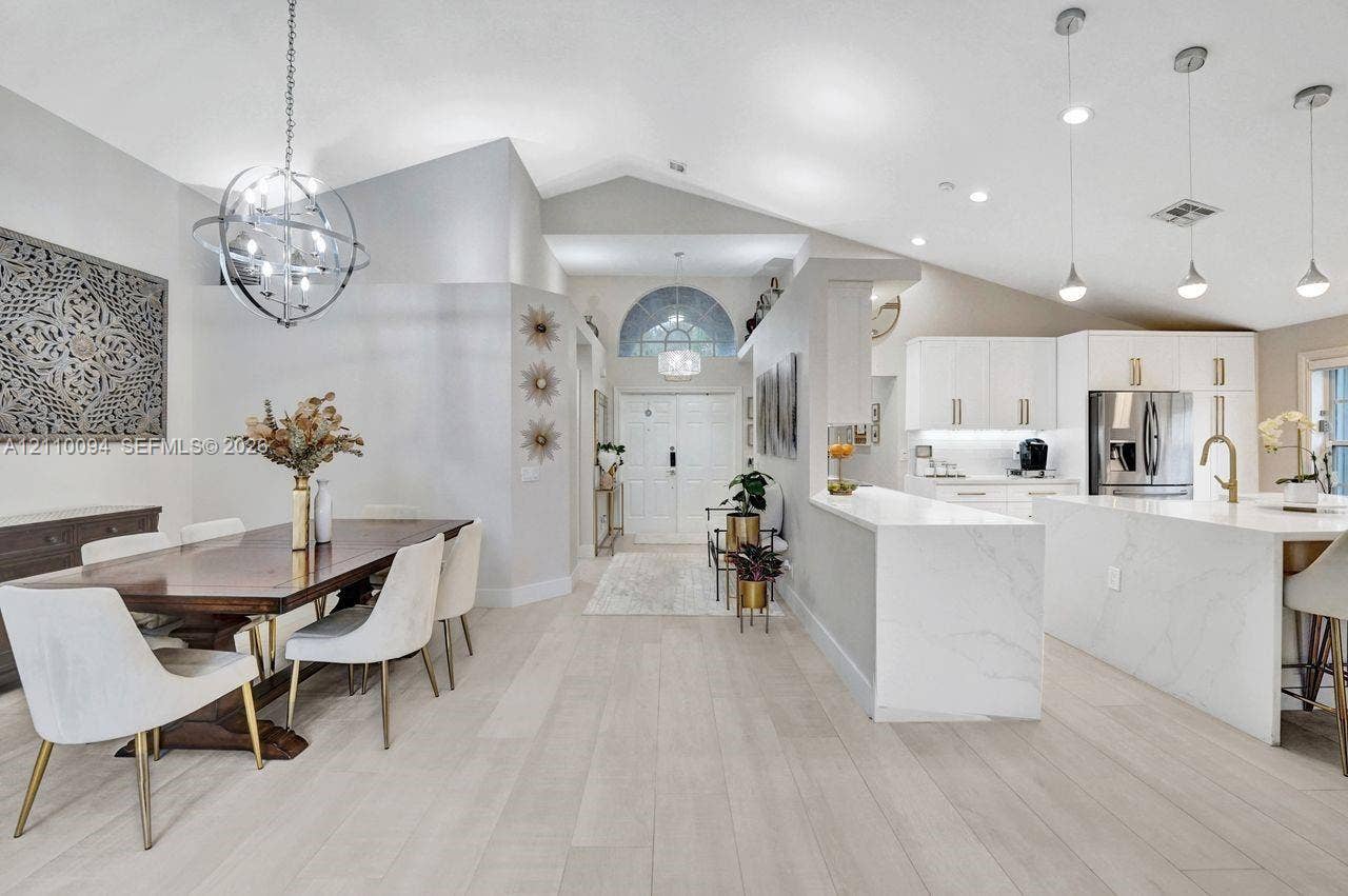 2064 Island Circle, Weston, FL 33326 Vaulted ceilings with recessed lighting, wood-finish flooring, a kitchen island with stone-finish waterfall edges, white cabinetry, and a spherical metal chandelier