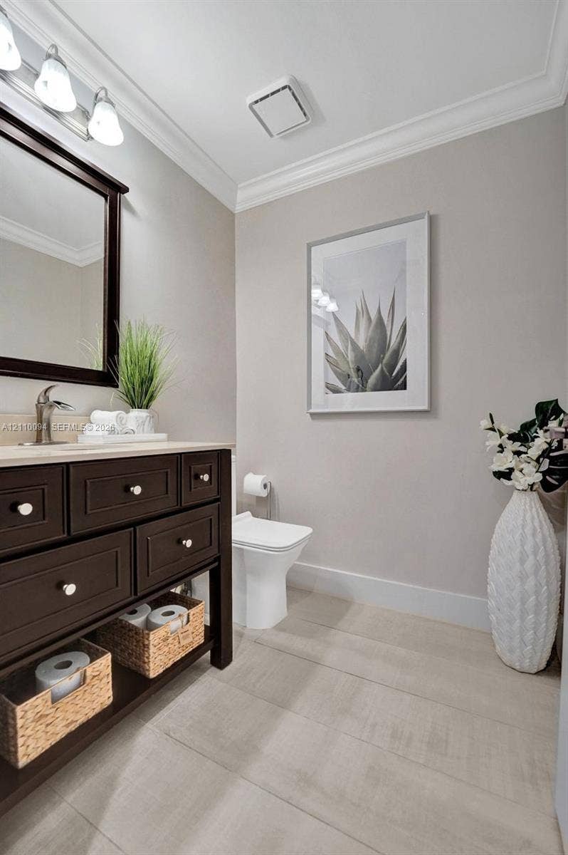 2064 Island Circle, Weston, FL 33326 Dark-finish vanity cabinet, neutral stone-top surface, brushed metal faucet, three-bulb vanity lighting, and crown molding