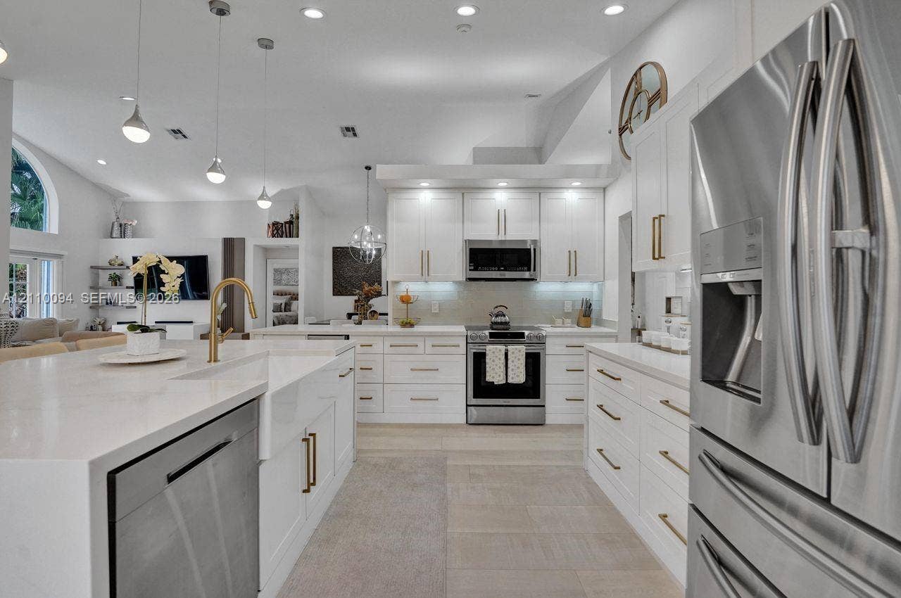 2064 Island Circle, Weston, FL 33326 Kitchen featuring white shaker-style cabinetry with gold-toned hardware, quartz countertops, a farmhouse-style apron-front sink, stainless steel appliances, and pendant lighting