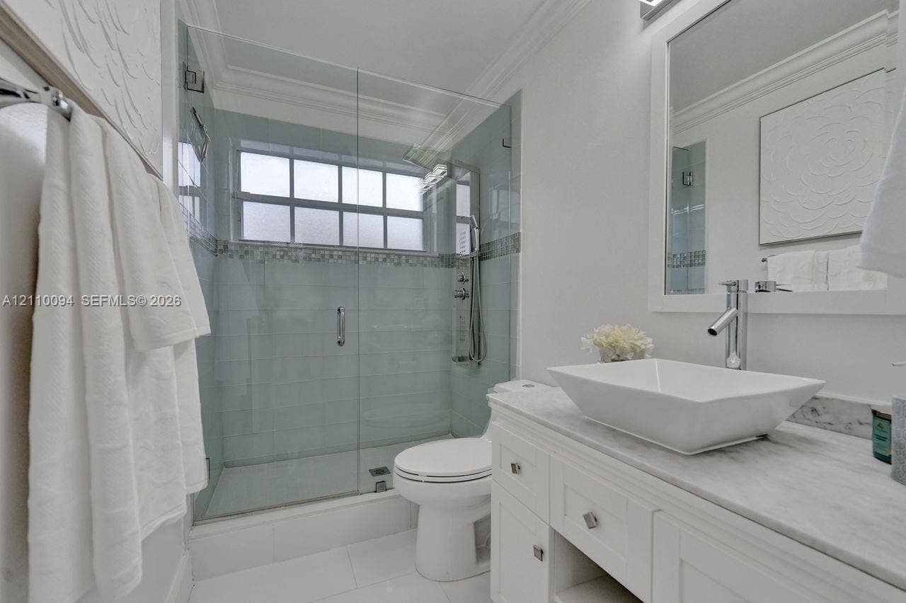 2064 Island Circle, Weston, FL 33326 White vanity with a stone countertop, rectangular vessel sink, frameless glass-enclosed shower featuring mosaic tile accents, and a fixed-pane window