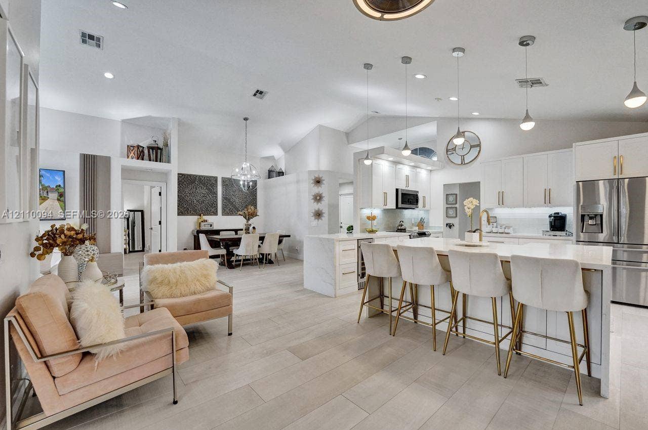 2064 Island Circle, Weston, FL 33326 Open-concept living space featuring vaulted ceilings, wood-finish flooring, a kitchen island with stone-surface countertop, white shaker-style cabinetry, and recessed lighting
