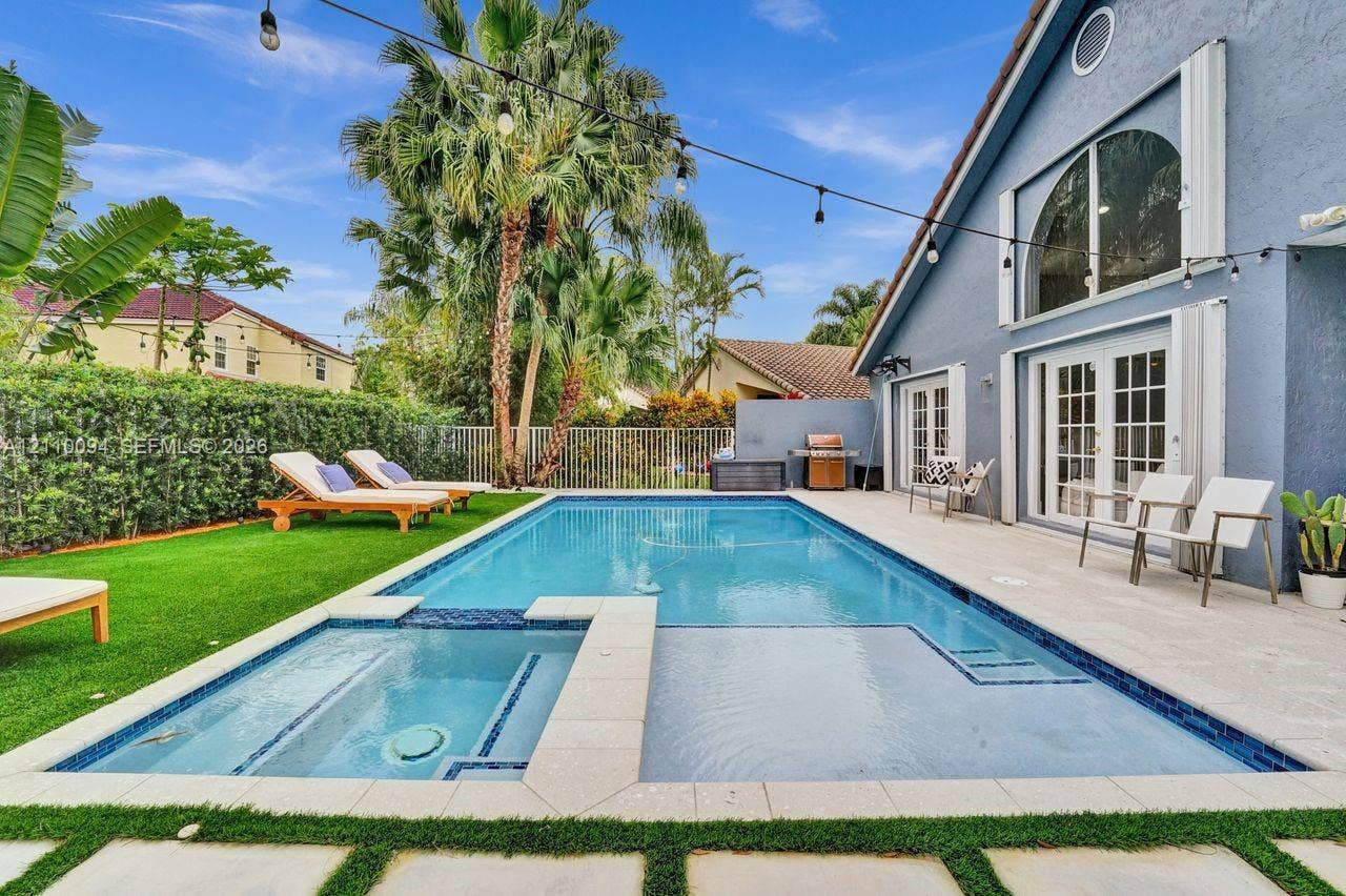 2064 Island Circle, Weston, FL 33326 Backyard pool area featuring an integrated spa, stone-paver decking, artificial turf lawn, and arched window detailing on the exterior facade