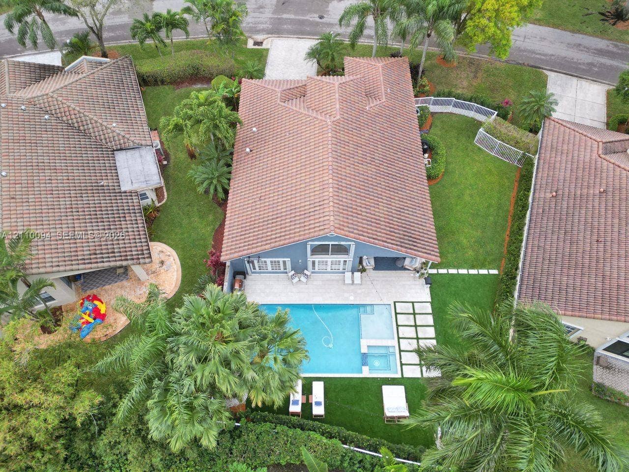 2064 Island Circle, Weston, FL 33326 Aerial perspective of a property featuring a tile roof, an in-ground swimming pool with an integrated spa, expansive paver patio, and lush landscaping