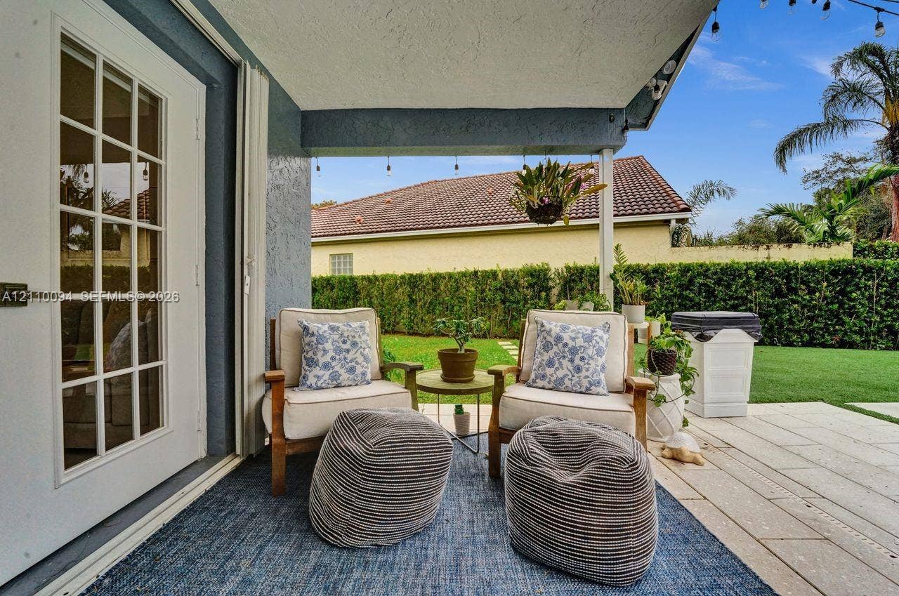 2064 Island Circle, Weston, FL 33326 Covered patio featuring large-format stone pavers, white French door access, and a privacy hedge enclosure
