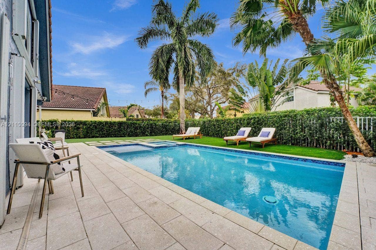 2064 Island Circle, Weston, FL 33326 Rectangular swimming pool featuring a built-in spa, stone paver decking, synthetic turf lawn, and mature palm trees