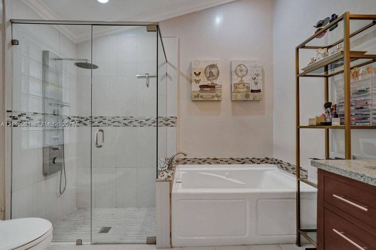 2064 Island Circle, Weston, FL 33326 Frameless glass shower enclosure with integrated rainfall shower head and body sprayers, soaking tub with a stone-composite surround, and decorative mosaic tile accents