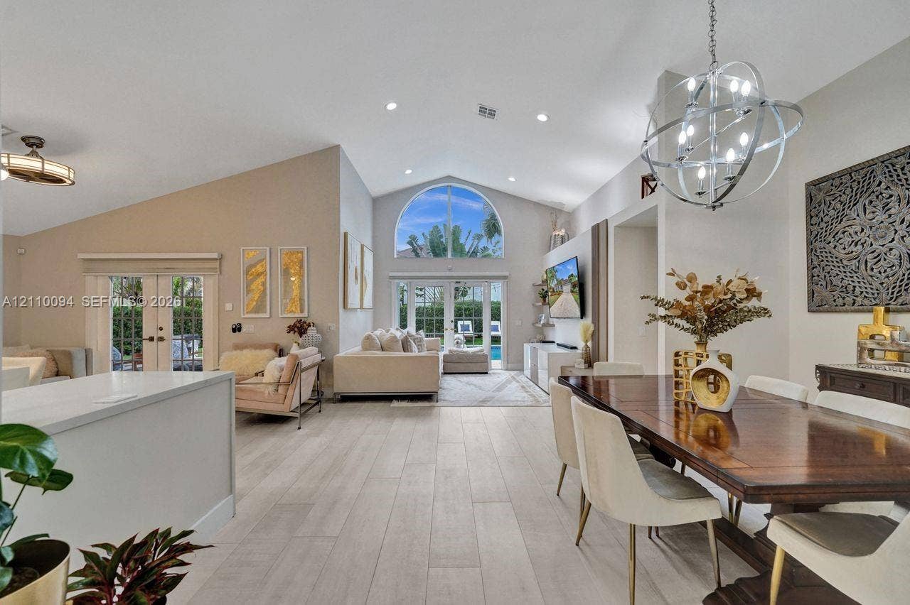 2064 Island Circle, Weston, FL 33326 Open-concept interior featuring vaulted ceilings, wood-finish flooring, a prominent arched window, and a spherical metal chandelier